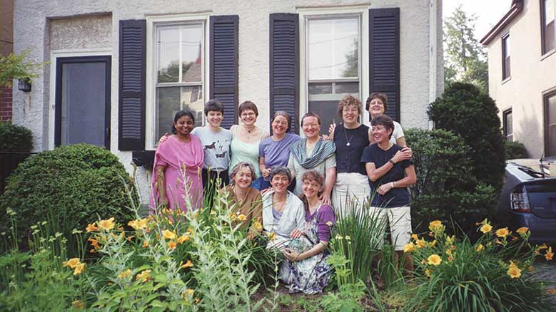 A group of women posing in a garden outside of a house.